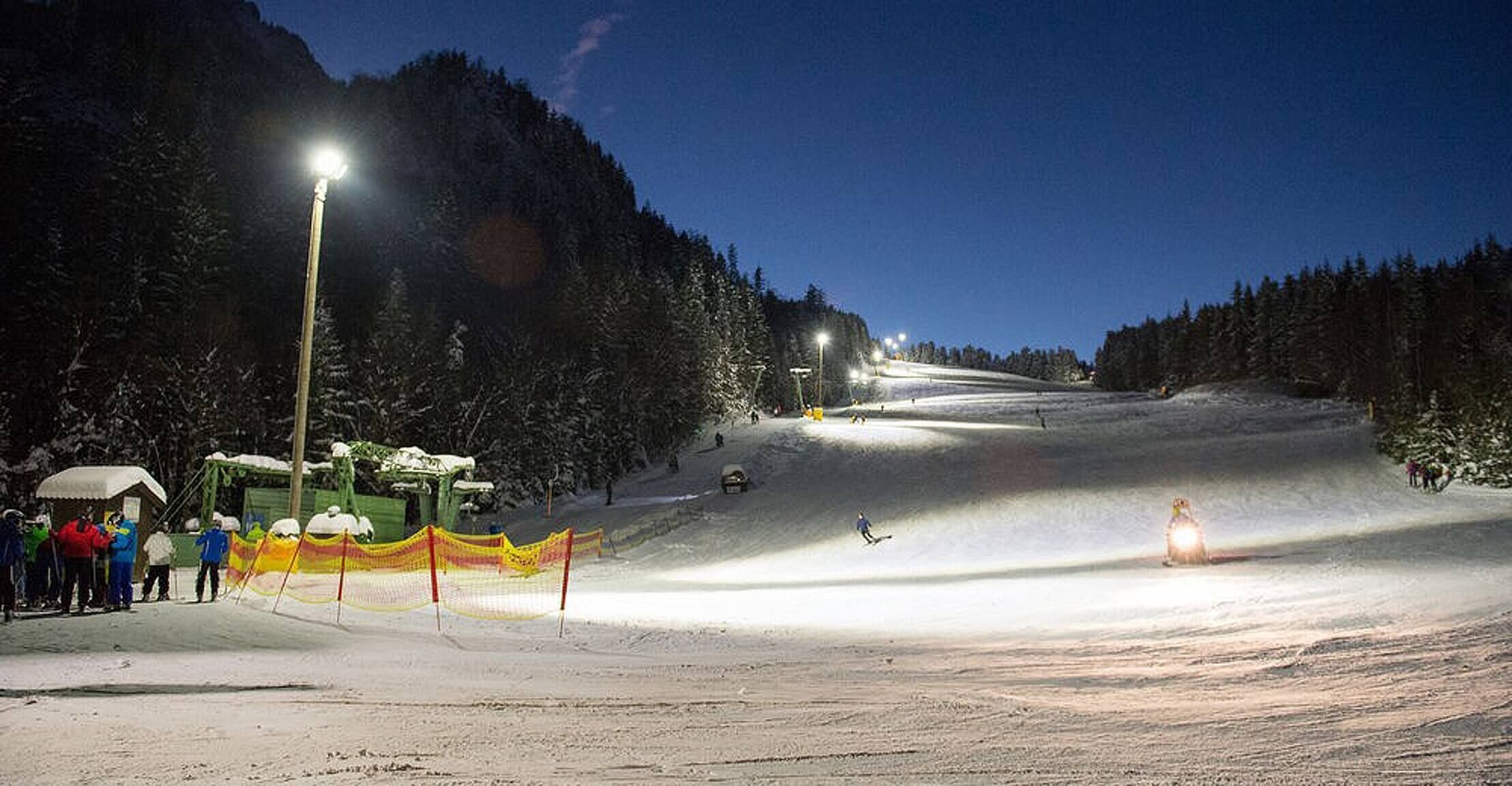 A snow-covered ski slope at night with artificial lighting.