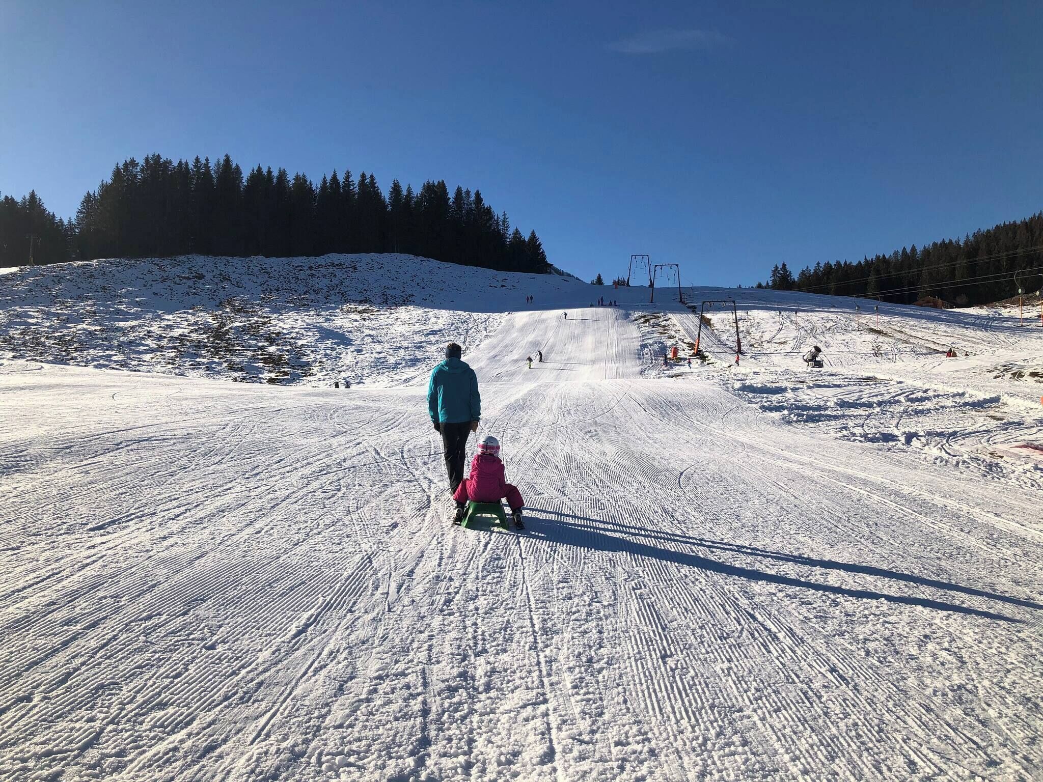 A snowy ski slope with a person and a child sledding.