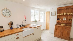 A kitchen with a wooden countertop, white cabinets, a sink, and a clock. - Kelsey (Truro)