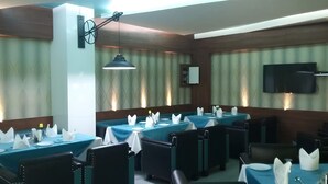 A restaurant with tables set for dining, a television mounted on the wall, and a hanging light fixture. - Club 7 (Bareilly)