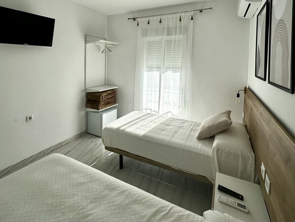 A minimalist bedroom with a bed, bedside table, and a mirror. - Hostal Merino Jédula (Arcos de la Frontera)