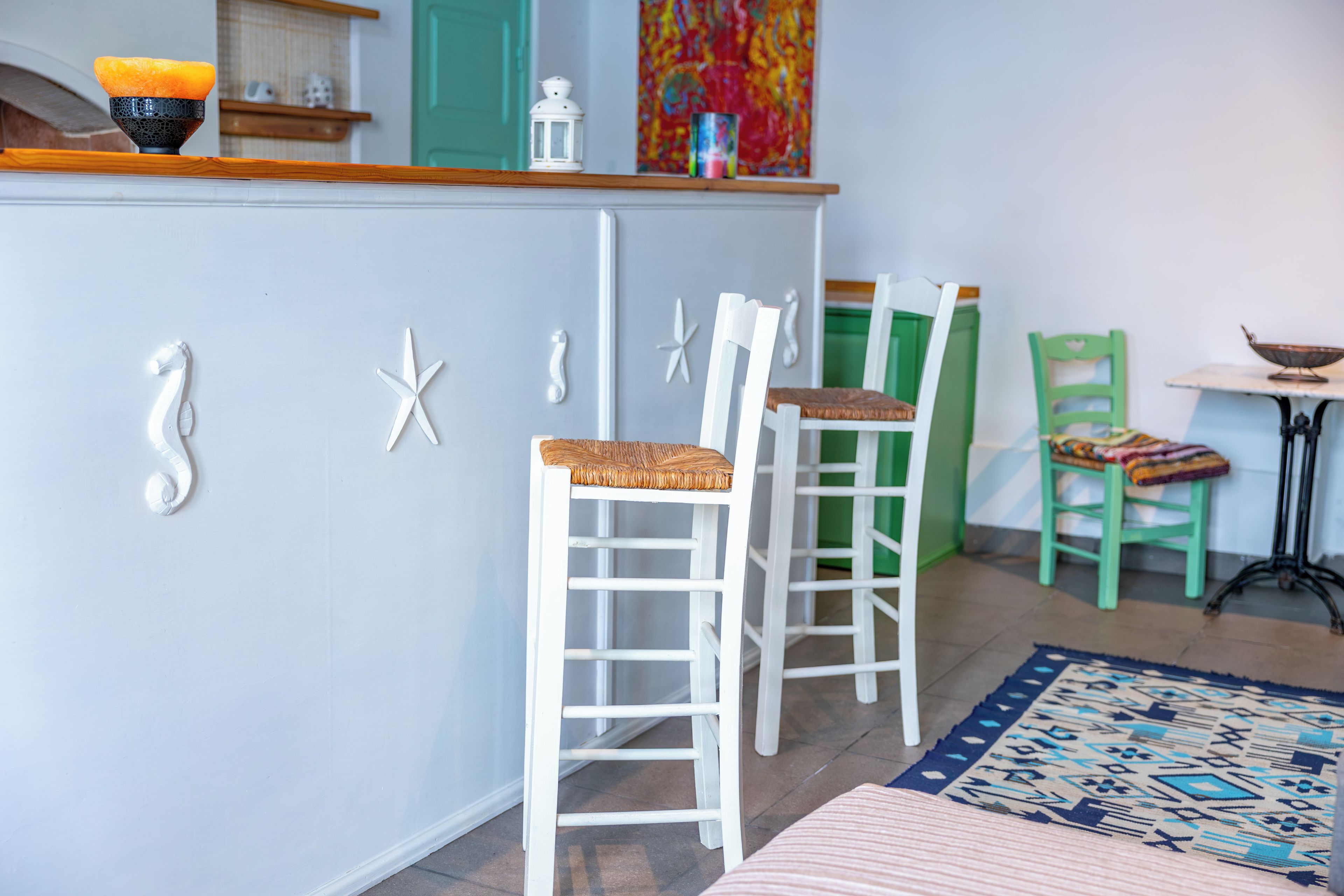 A room with a kitchen counter, white chairs, a green chair, a small table, and a patterned rug.