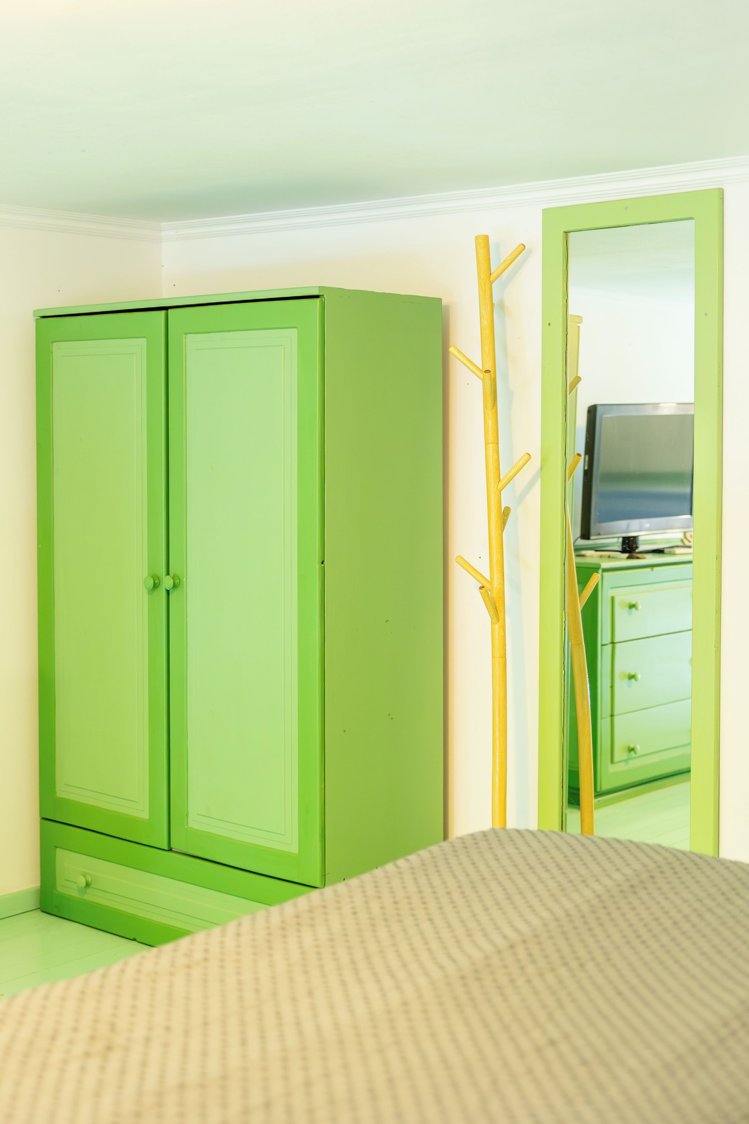 Ein Zimmer mit einem grünen Kleiderschrank, einem Bett mit gestreifter Bettwäsche und einem Spiegel, der einen Fernseher und eine Kommode reflektiert.