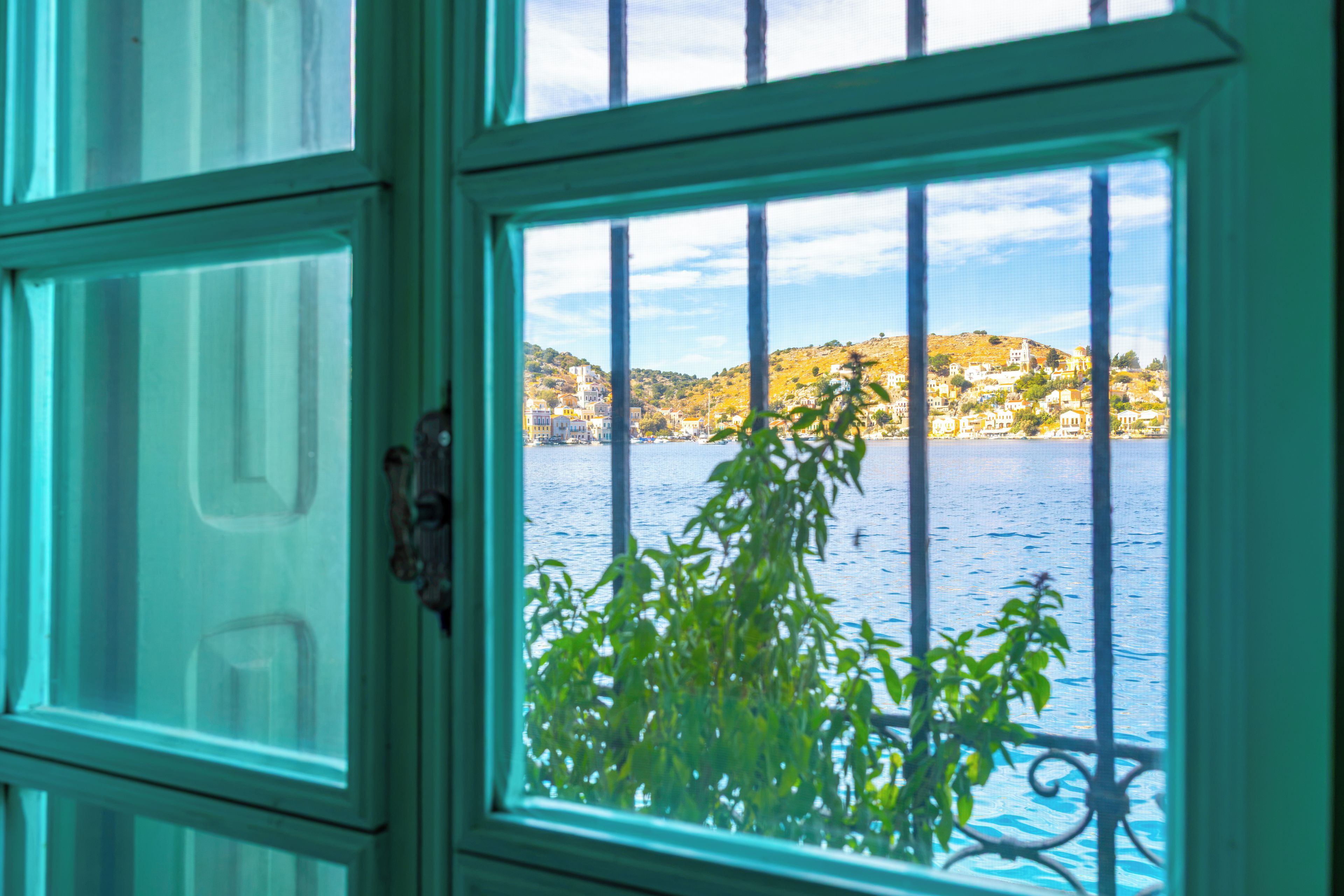 A window with metal bars, through which a view of a coastal town and water is visible.