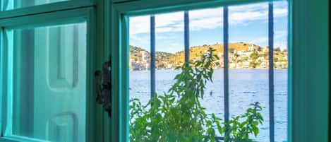 A window with metal bars, through which a view of a coastal town and water is visible.