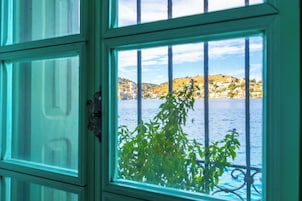 Una ventana con barrotes a través de los cuales se ve una vista de un pueblo costero y el agua.