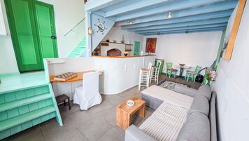Un espacio habitable compacto con kitchenette, un sofá, una mesa de comedor y una escalera.