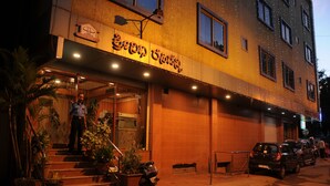 A building with a sign in a foreign script, a staircase with potted plants, and parked cars. - Srinidhi Residency (Bengaluru)