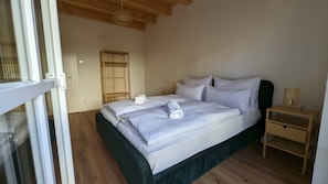 A bedroom with a bed, wooden headboard, bedside tables, and a wardrobe. - Liboria I Ferienwohnung am Riegsee mit Atemberaubendem Panoramablick! (Riegsee)