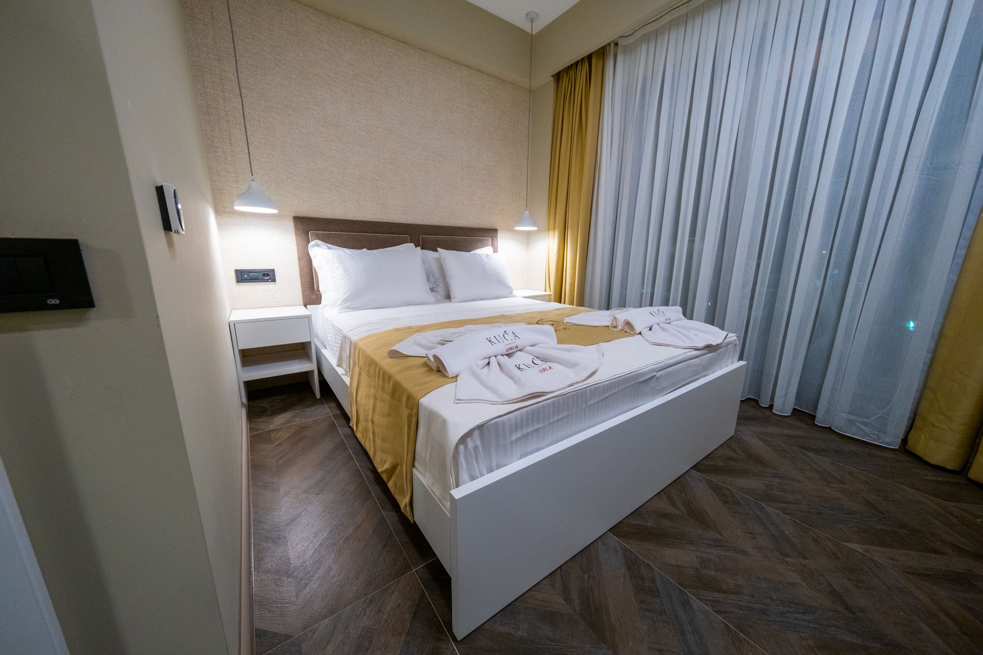 A hotel room with a bed, bedside tables, a lamp, and a window with curtains.