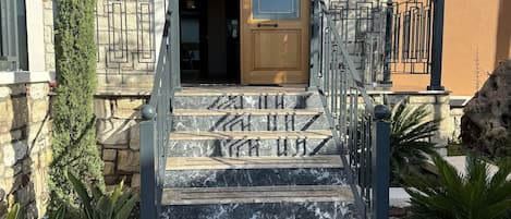 Un edificio de piedra con puerta de madera, una escalera con barandillas de metal y una guirnalda decorativa sobre la puerta.