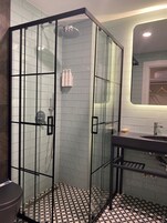 Un baño moderno con ducha de vidrio, un lavamanos y piso de baldosas.