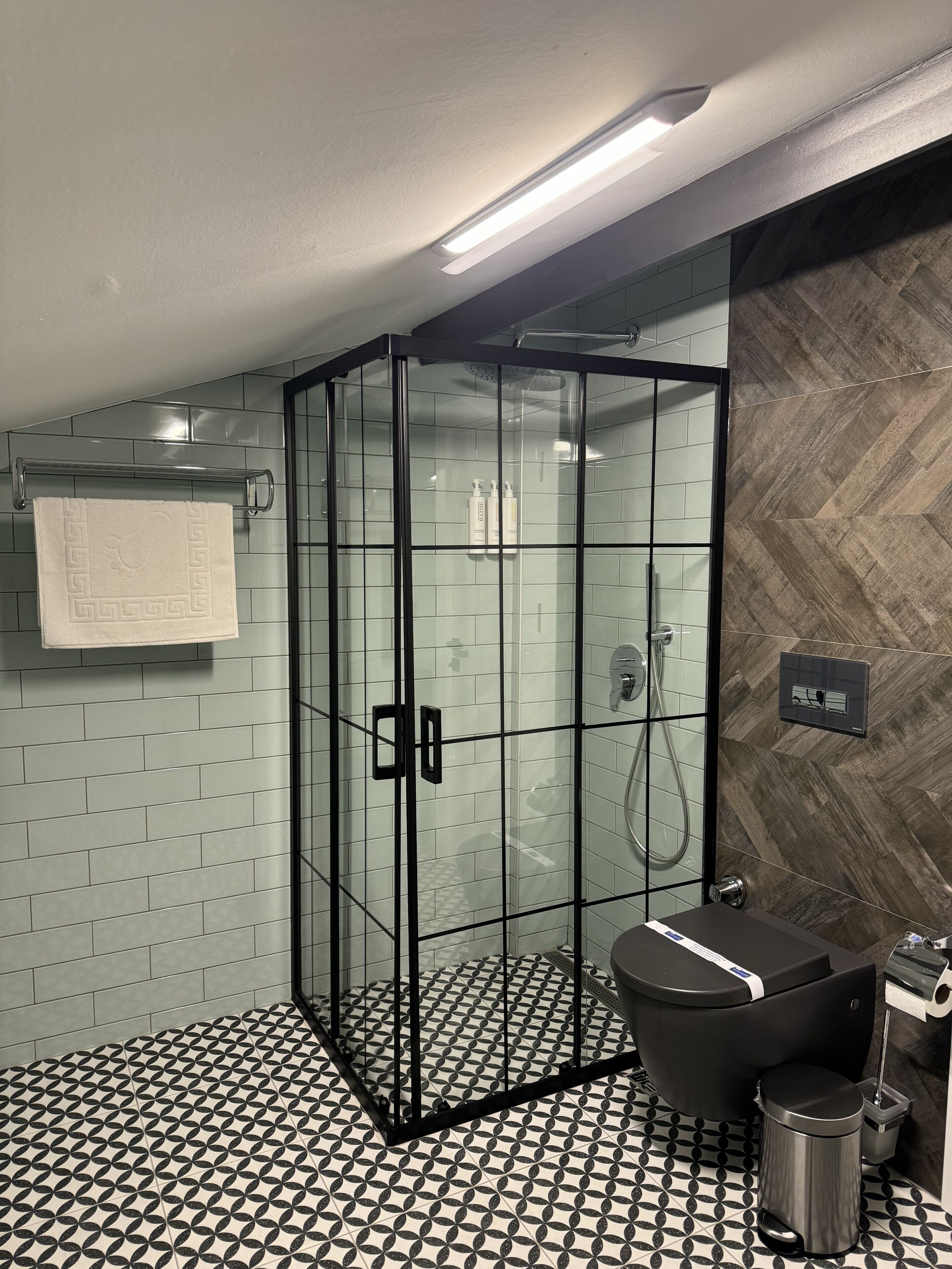 A modern bathroom with a glass-enclosed shower, a black toilet, and a patterned floor.