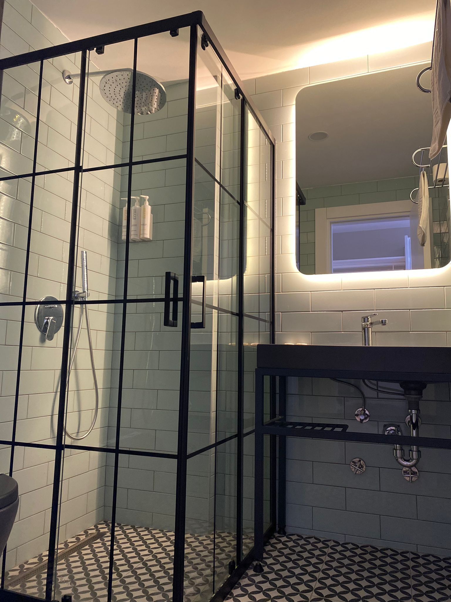 Un baño moderno con cabina de ducha de vidrio, lavamanos negro y suelo de baldosas.