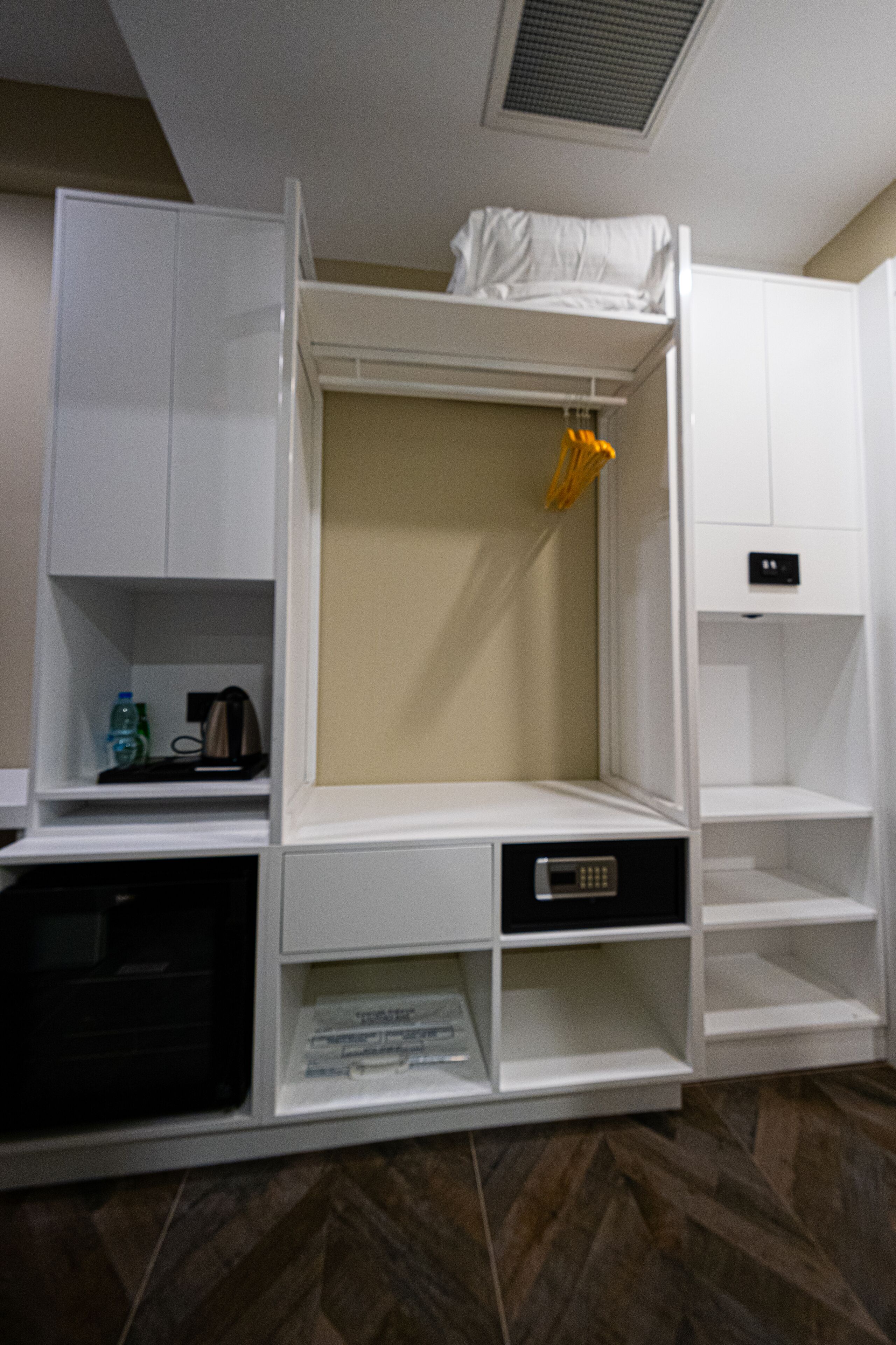 Habitación de hotel con cama empotrada, un pequeño escritorio y una estantería con una botella de agua y una cafetera.