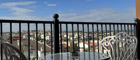 A balcony with a table and chairs, overlooking a cityscape with buildings and a clear sky.