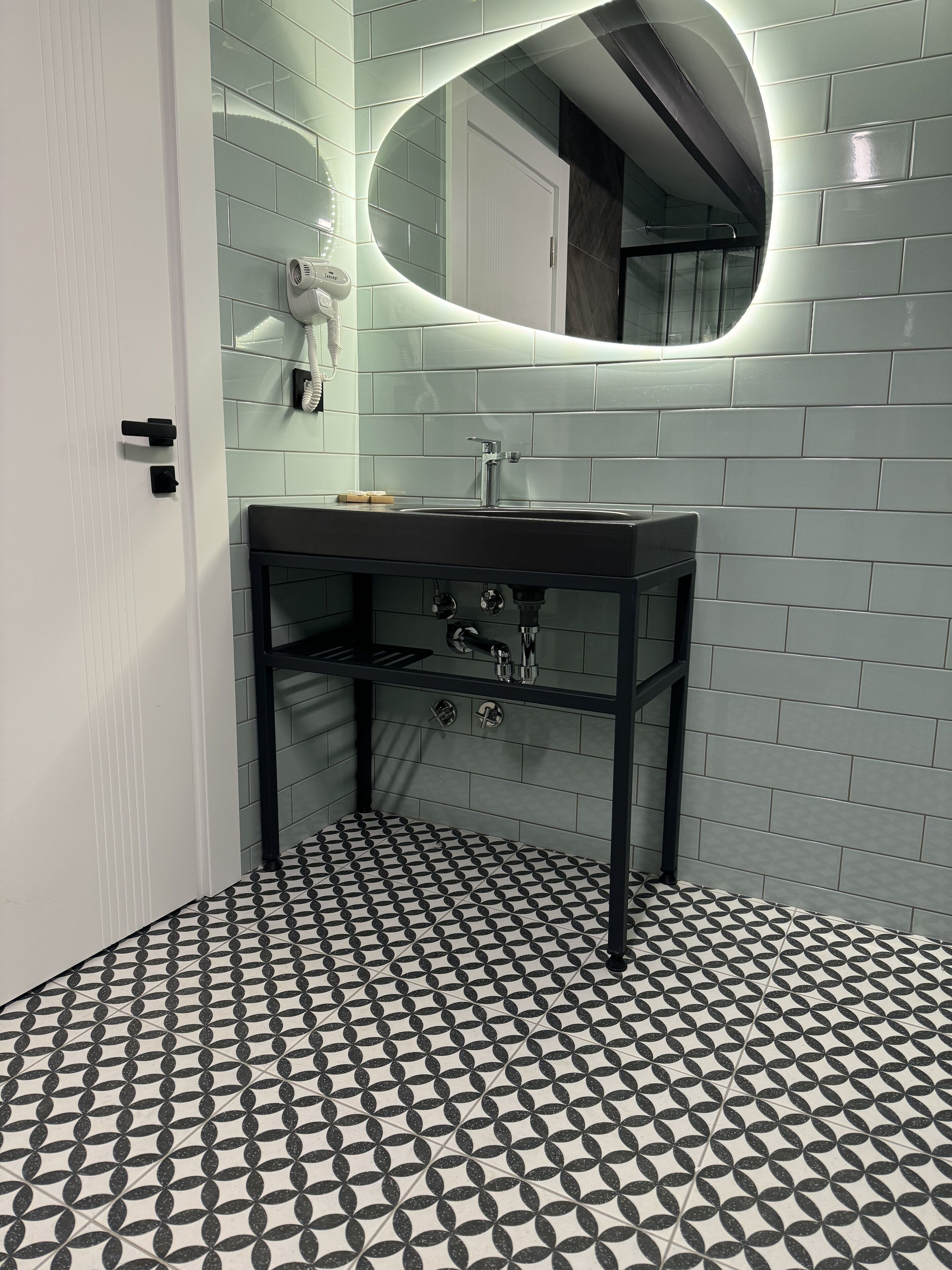 Une salle de bain moderne avec un lavabo noir, un miroir et un carrelage à motifs.