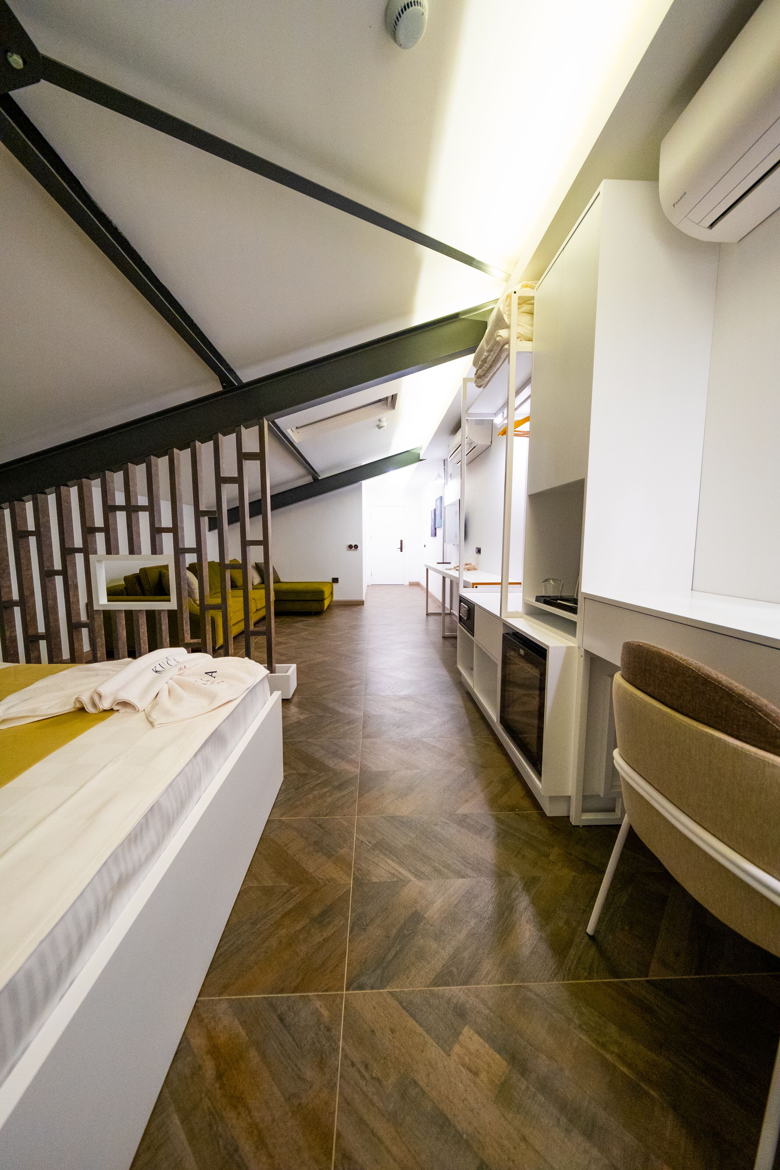 A modern loft bedroom with a sloped ceiling, built-in seating, and a kitchenette.