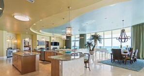 A spacious kitchen with a large island, modern pendant lighting, and a view of the ocean through large windows. - Turquoise Place 2304D Penthouse by Liquid Life | 8,000 SqFt Balcony (Orange Beach)