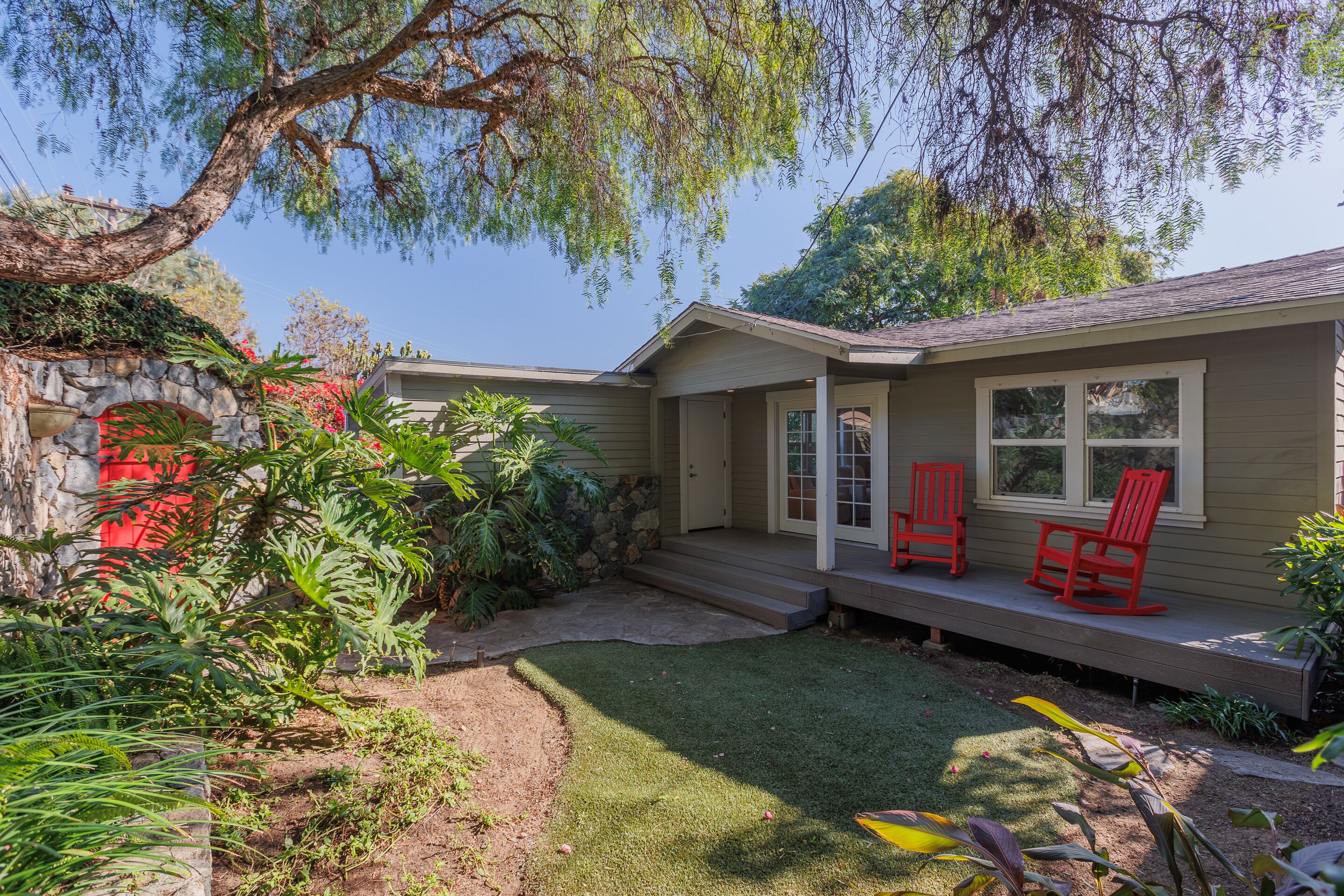 A house with a stone archway, a porch with red chairs, and a well-maintained lawn.