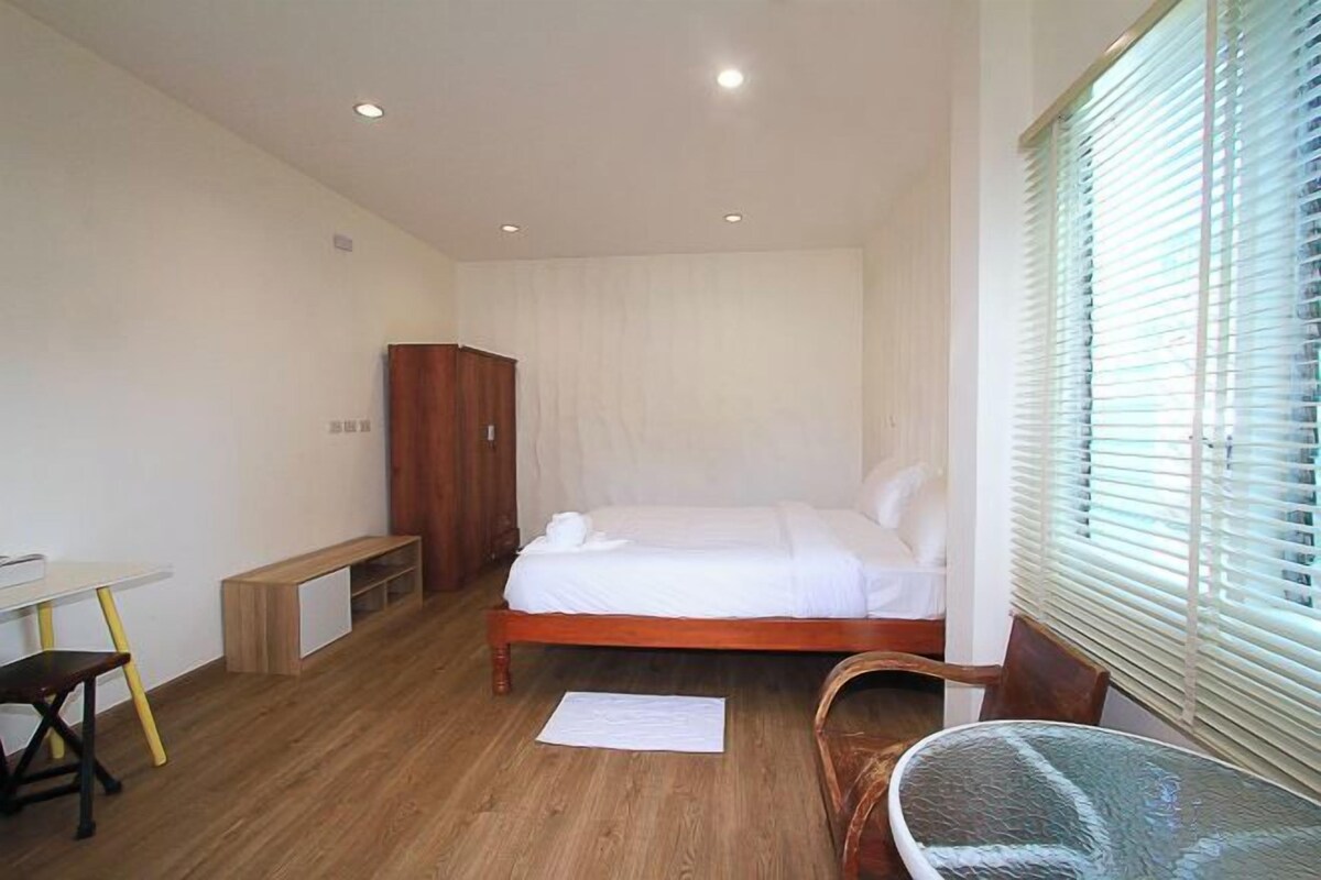 Un dormitorio con cama, escritorio, silla, armario y ventana con persianas.
