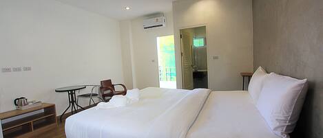 A neatly made bed in a hotel room with a wooden headboard, a small table with a chair, and an air conditioning unit on the wall.