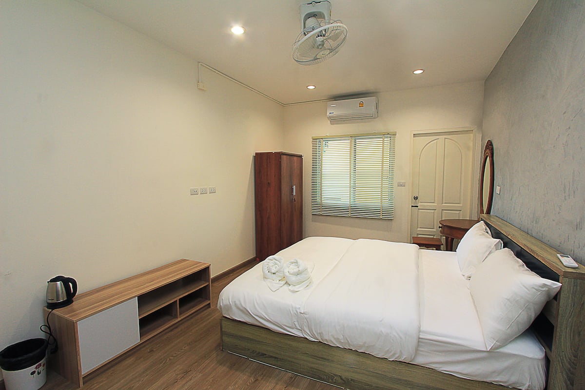 Quarto bem arrumado com cama, um armário de madeira, uma mesinha e uma janela com persianas.