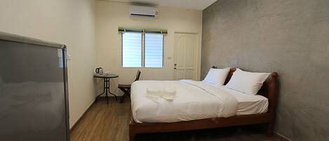 A bedroom with a bed, a desk, a chair, and a refrigerator.