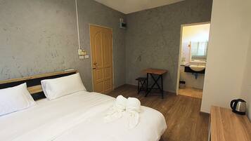 Habitación de hotel con cama, puerta de madera, una mesita y baño visible a través de una puerta abierta.