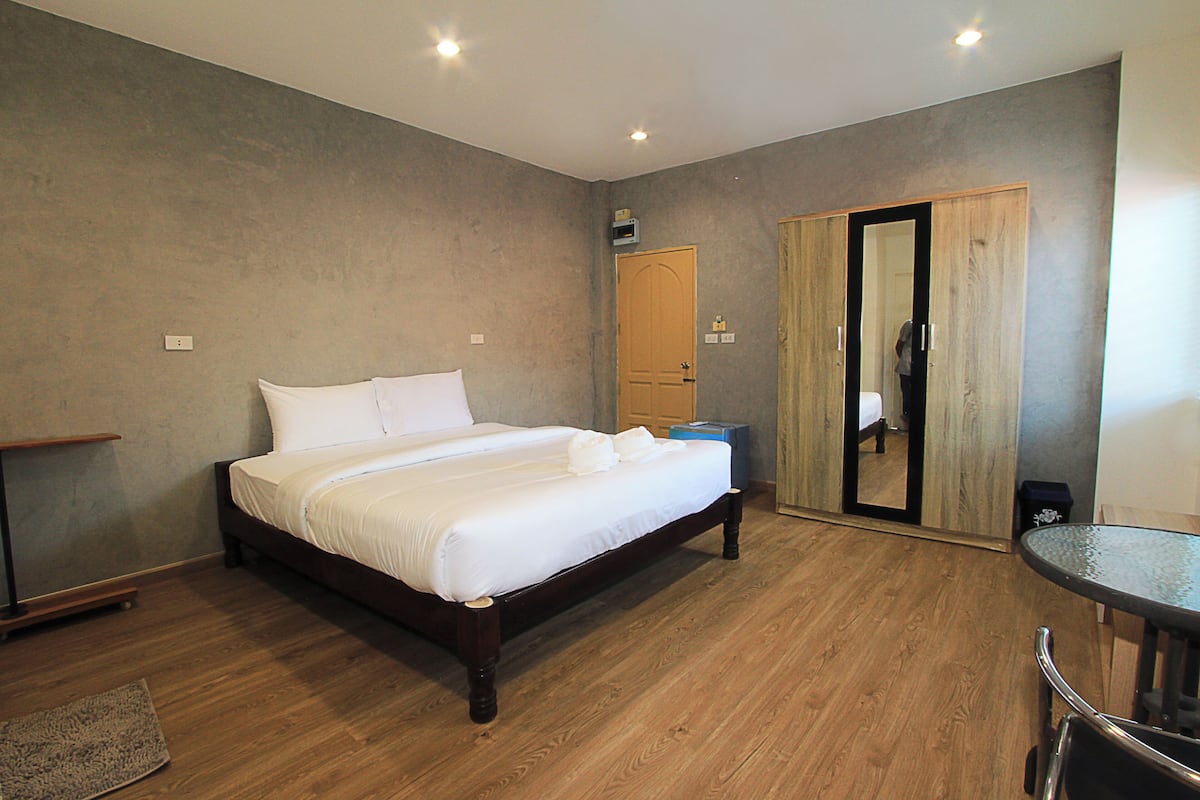 Quarto com cama de madeira, uma mesinha, espelho e guarda-roupa.