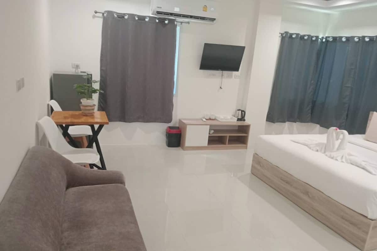 Quarto de hotel moderno com sofá, pequena mesa de jantar, televisão na parede e cama com travesseiro em forma de cisne.