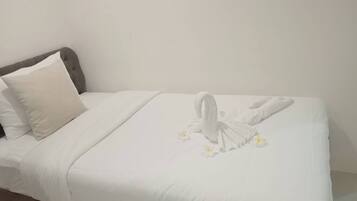 A neatly made bed with white bedding and a swan-shaped towel arrangement.