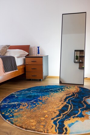 Quarto com cama, mesa de cabeceira, cômoda, espelho grande e tapete azul estampado.