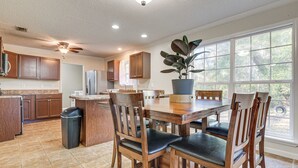 A spacious kitchen with wooden cabinets, a dining table with chairs, a ceiling fan, and a large window with a view of greenery. - Tranquil Coden Retreat: 10 Mi to Dauphin Island! (Theodore)