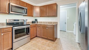 A kitchen with wooden cabinets, stainless steel appliances, and a tiled floor. - Tranquil Coden Retreat: 10 Mi to Dauphin Island! (Theodore)