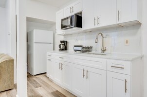 Una cocina moderna con armarios blancos, microondas integrado, cafetera y lavamanos.