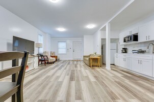 Una cocina moderna con armarios blancos, un microondas y una cafetera. Hay una mesa de comedor de madera con sillas y un sofá en la sala.