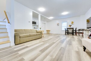 Amplia sala de estar con sofá color beige, piso de madera, una mesa de comedor con sillas y una cocina al fondo.