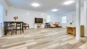 Uma sala de estar ampla com piso de madeira, televisão, lareira e área de jantar com cadeiras e mesa.