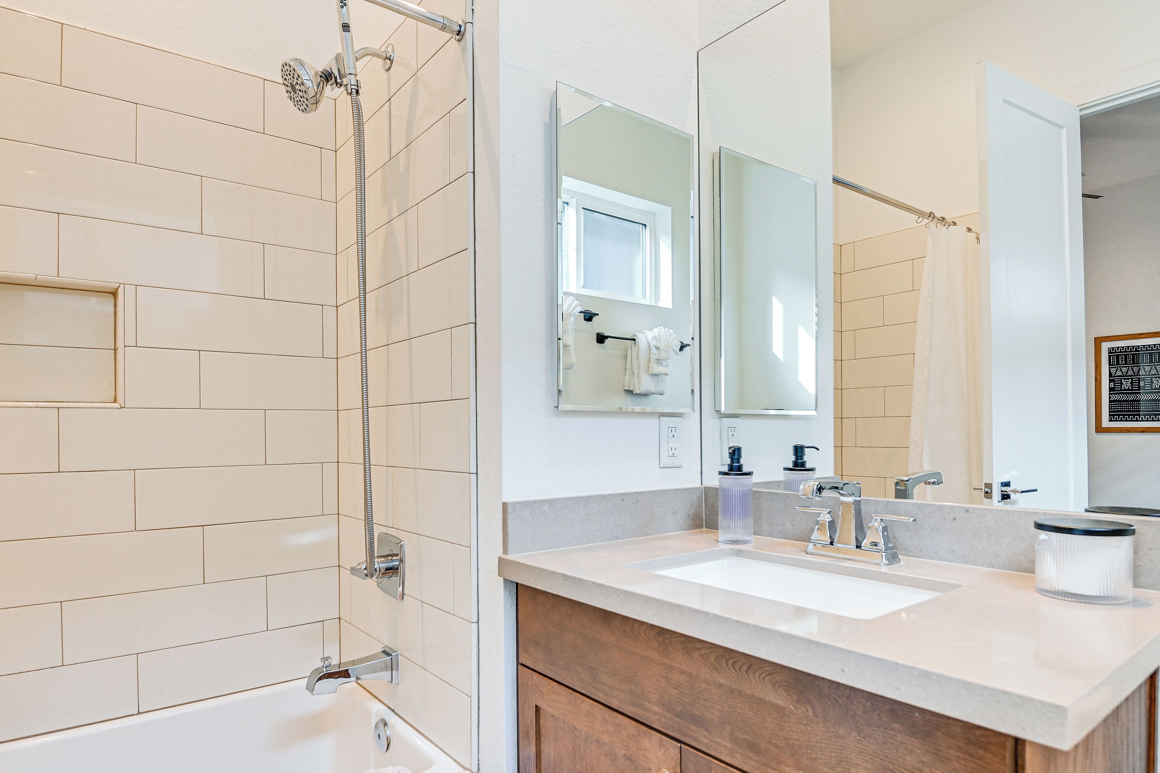 A modern bathroom with a bathtub, a shower with a handheld showerhead, a sink with a mirror, and a towel rack.