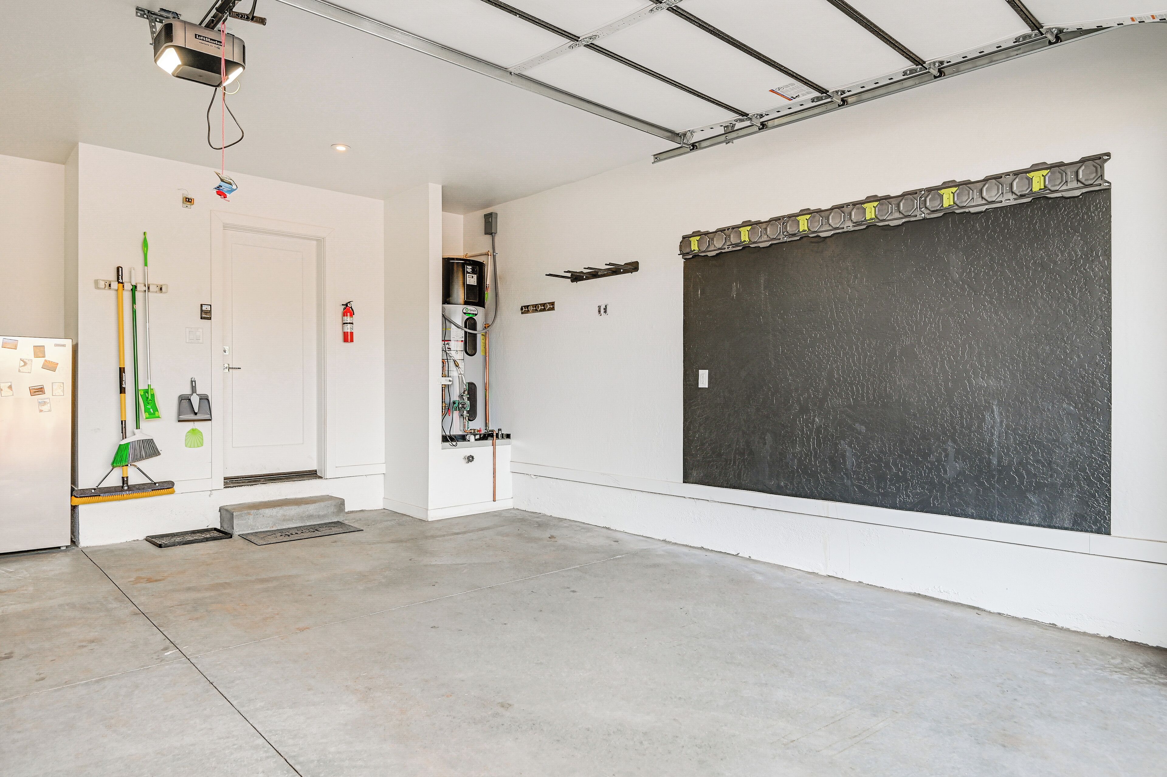 Una habitación limpia de estilo industrial, con una pizarra grande, una puerta blanca y diversas herramientas de limpieza en la pared.
