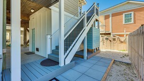 Ein Wohngebäude mit einer Holzterrasse, einer Treppe zu einer überdachten Veranda und einem eingezäunten Garten.