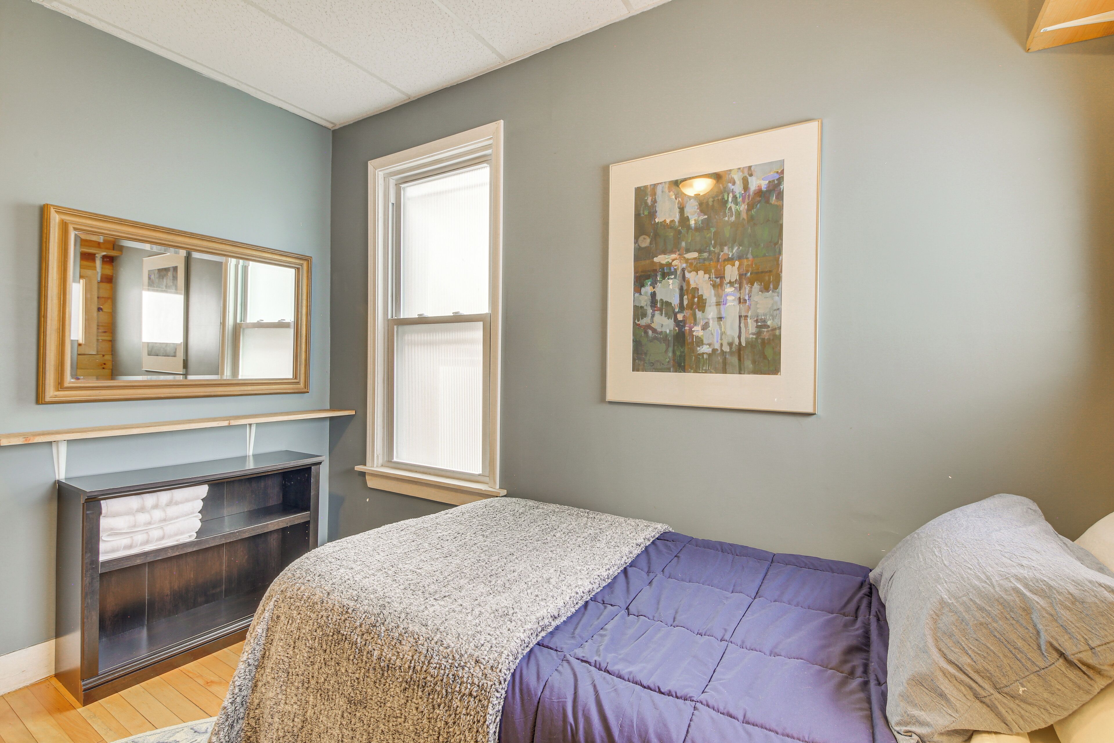 A bedroom with a bed, a dresser, a window, and a painting on the wall.