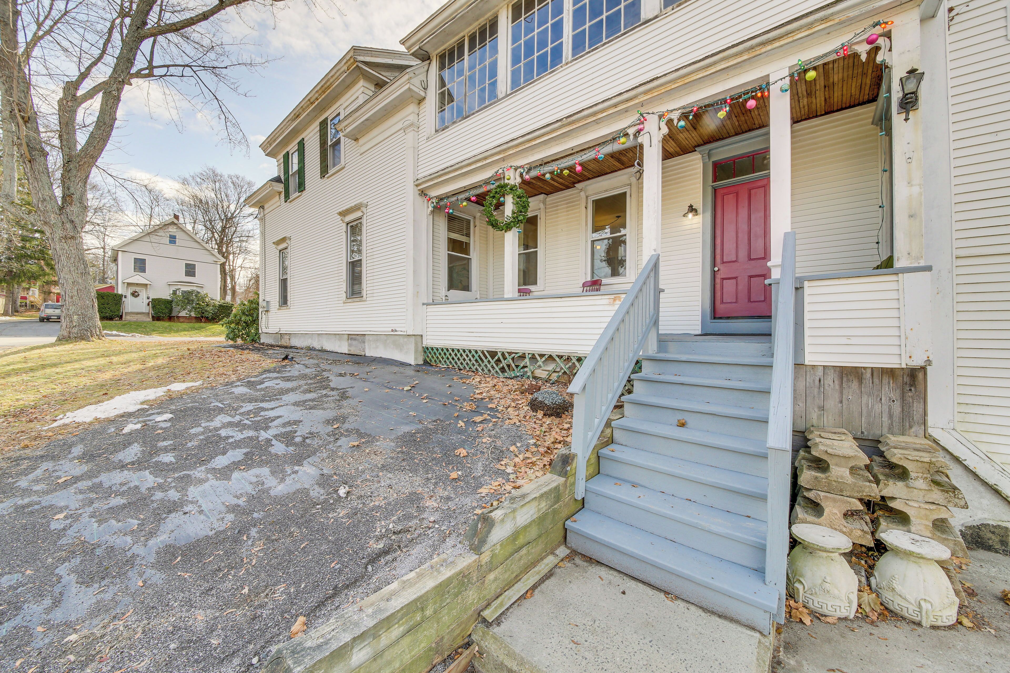 A two-story house with a front porch, a red door, and a staircase leading to the entrance.