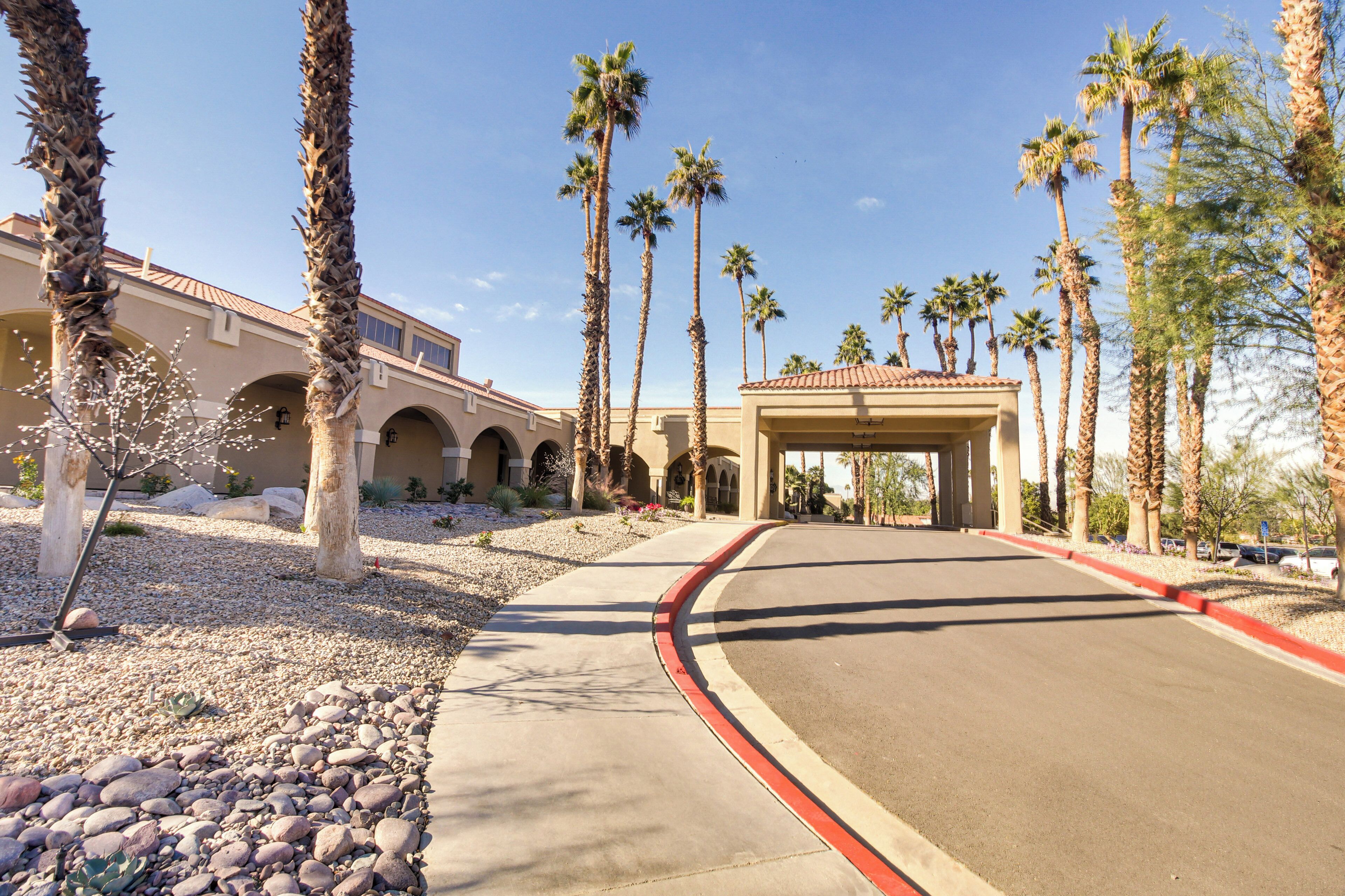 A hotel entrance with palm trees, a curved driveway, and a covered walkway.