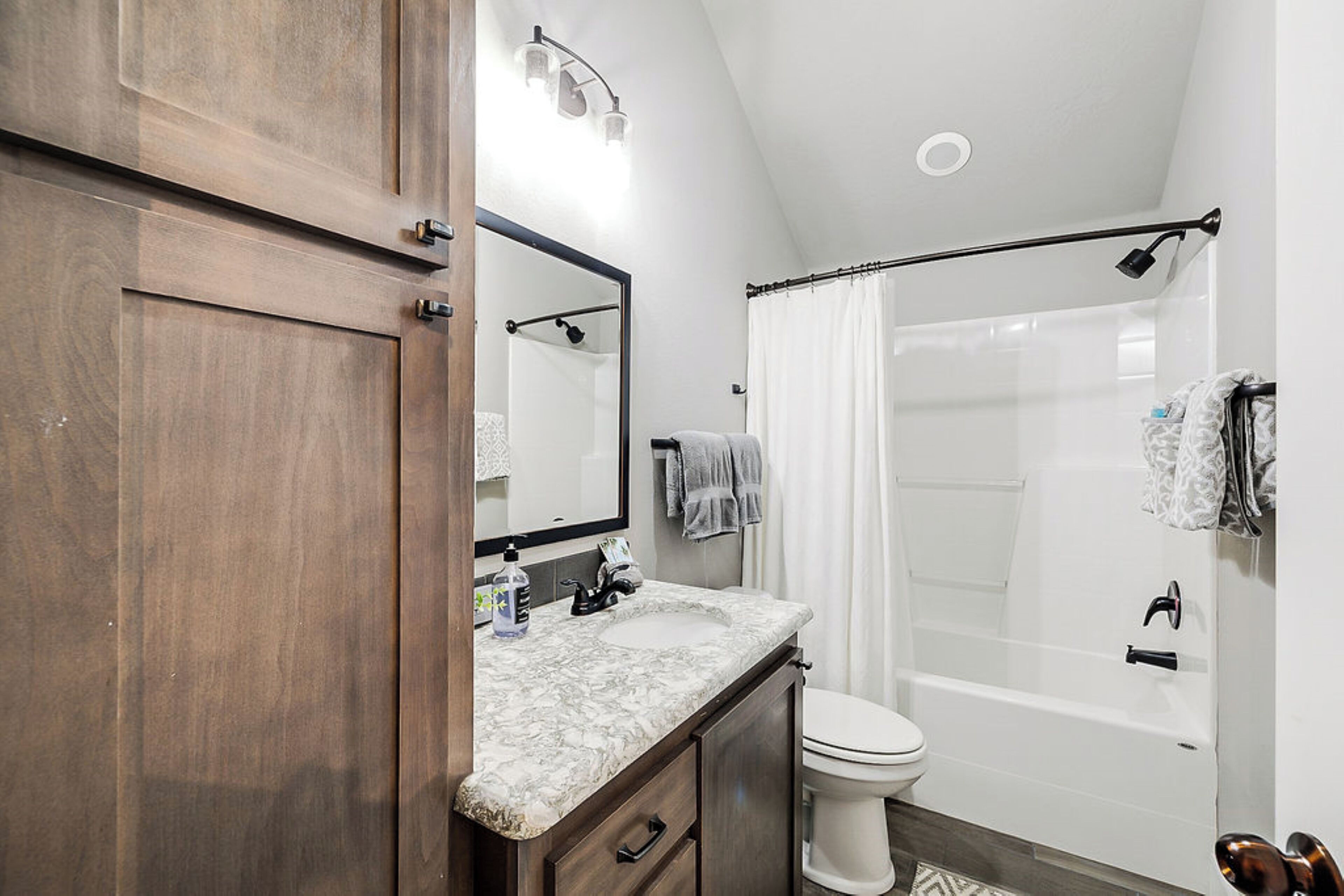 A bathroom with a wooden vanity, a white sink, a mirror, a toilet, and a shower area with a curtain.