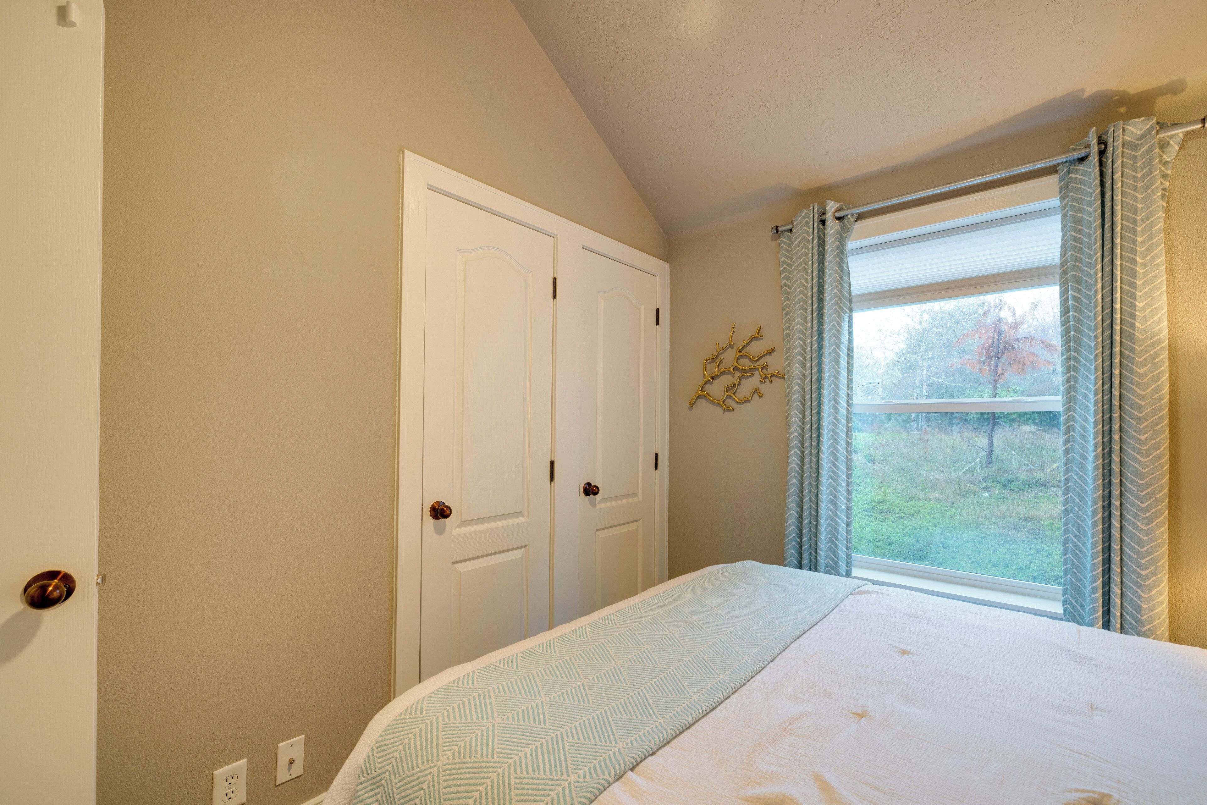 A bedroom with a bed, a window with curtains, a door, and a wall-mounted decoration.