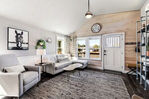 A modern living room with a sectional sofa, a coffee table, a wall-mounted clock, and a large window with shutters.