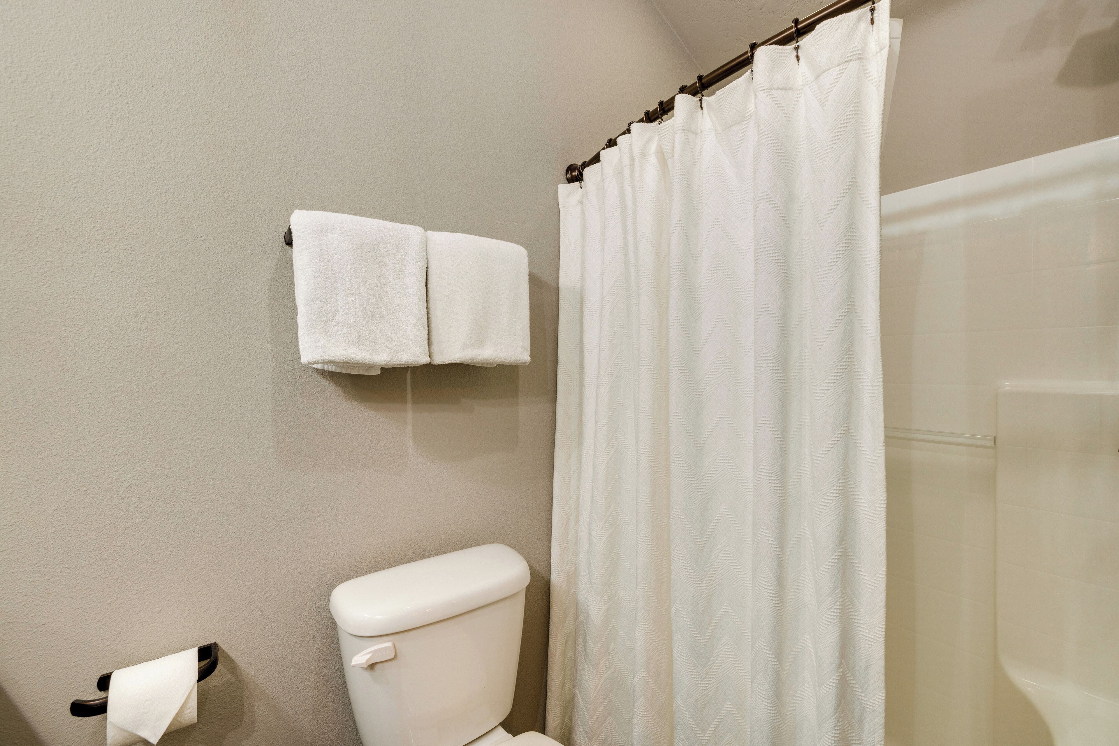 A bathroom with a toilet, a towel rack with two towels, and a shower curtain.