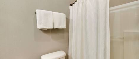A bathroom with a toilet, a towel rack with two towels, and a shower curtain.